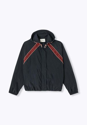 Coupe-vent noir à capuche avec poignets élastiques, rayures diagonales rouges et beiges sur la poitrine, et fermeture éclair à l'avant.