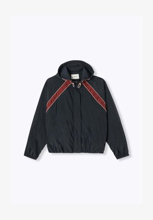 Coupe-vent noir à capuche avec poignets élastiques, rayures diagonales rouges et beiges sur la poitrine, et fermeture éclair à l'avant.