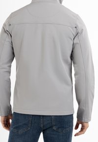 Veste softshell grise à coupe droite, dotée d'un col, avec des accents de couture visibles et une texture lisse. Portée avec un jean bleu.