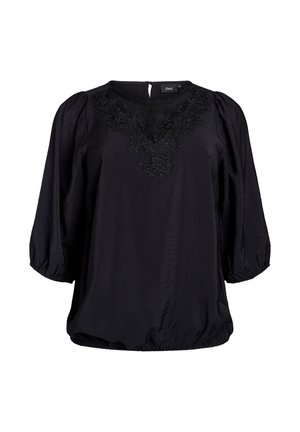 Melna blūze ar pūksteniem piedurknēm, noapaļotu apkakli un sarežģītu melnu iešuvumu uz krūšu. Mīksta tekstūra un elastīgs apakšmala.