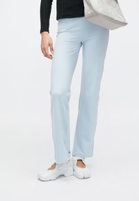 Svetlomodré pružné nohavice s priliehavým strihom a miernym rozšírením na spodku, v kombinácii s bielou obuvou. Hladký, priedušný materiál.