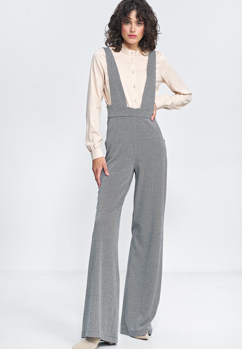 Szare ogrodniczki w wzór hounds-tooth mają szerokie nogawki i regulowane ramiączka, połączone z beżową koszulą z guzikami. Tkanina ma strukturalne wykończenie.