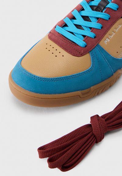 Πολύχρωμο αθλητικό παπούτσι με ταμπά δέρμα, μπλε σουέντ, μπορντό λεπτομέρειες, μπλε κορδόνια και επιπλέον δεμένα μπορντό κορδόνια σε λευκό φόντο.