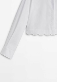 Blouse blanche à manches longues, ourlet festonné et texture lisse. Comprend un col classique et une fermeture à boutons sur le devant.