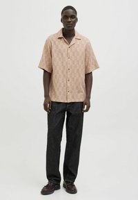 Chemise à manches courtes, boutonnée, de couleur orange clair avec un motif en chevron, associée à un jean foncé et des chaussures à lacets sombres.