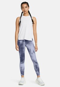 Un haut de sport sans manches blanc associé à un legging bleu tie-dye. La tenue présente une coupe décontractée et un tissu qui évacue l'humidité. Des baskets blanches.