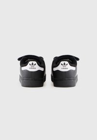 Baskets noires en suédine et cuir, avec un logo Adidas blanc et trois bandes sur le talon, semelle en caoutchouc et design à lacets.