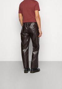 Pantalones de cuero marrón con un corte relajado, que cuentan con una cinturilla y bolsillos sutiles, combinados con una camisa de manga corta color marrón oscuro.