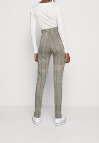 Pantalones de cuadros de talle alto en blanco y negro, de corte ajustado y con una textura suave, combinados con zapatillas blancas, vistos desde la parte de atrás.