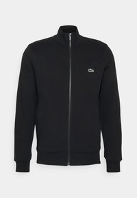 Veste noire à fermeture éclair avec col montant et petit logo crocodile vert sur le côté gauche de la poitrine, manches longues, poignets et ourlet côtelés.