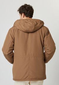 Giacca marrone con cappuccio, caratterizzata da una texture liscia e opaca, con una vestibilità leggermente rilassata, cuciture visibili e senza motivi o accenti distintivi.