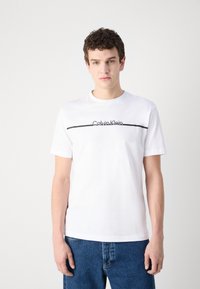 Hvid bomulds t-shirt med en sort vandret linje og "Calvin Klein" logo. Korte ærmer og rund halsudskæring. Standard pasform.