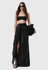 Top bandeau nero con arricciature, abbinato a una lunga gonna stratificata con spacchi alti. Gli accessori comprendono una borsa coordinata e occhiali da sole.