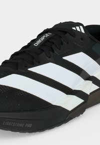 Αθλητικό παπούτσι Adidas σε μαύρο και άσπρο με τρεις λευκές ρίγες, μαύρα κορδόνια και λογότυπο τεχνολογίας σόλας Lightstrike Pro.