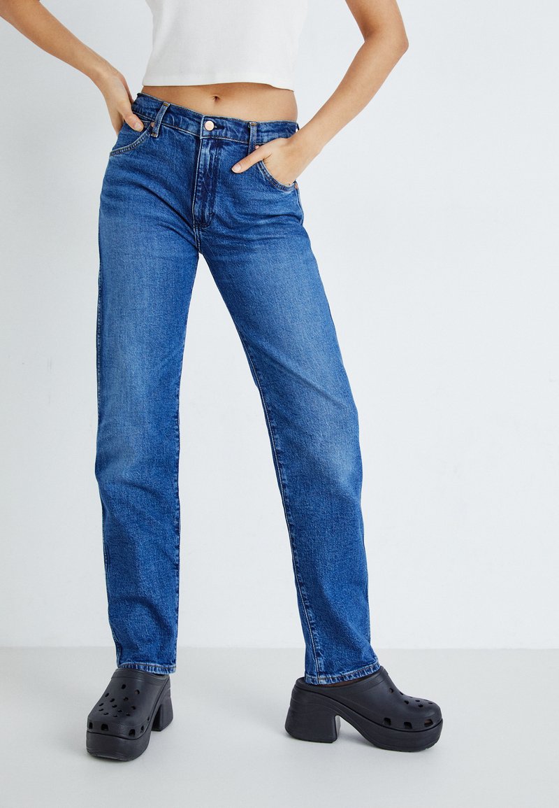 Blauwe denim straight-leg jeans met vijf zakken, een ritssluiting en een knoopsluiting. Draag ze met zwarte plateauhakken met ventilatiegaten.