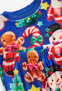 Tissu bleu ornée de motifs de Noël colorés, y compris des bonhommes en pain d'épice, des cannes en sucre d'orge et des bonhommes de neige. Ceinture élastique incluse.