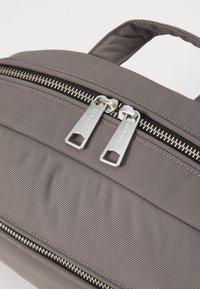 Borsa in tessuto grigio con una texture liscia, doppie cerniere argento e una maniglia sulla parte superiore. La borsa presenta cuciture visibili e un design elegante.