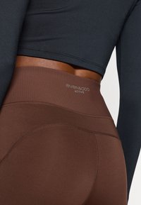 Activewear legging in een rijke bruine stof met een geribbelde tailleband. Voorzien van platgestikte naden en merkdetail op de tailleband.