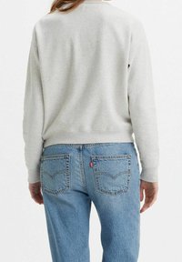 Felpa di cotone grigia con colletto a girocollo e polsini a costine, abbinata a jeans in denim azzurro chiaro con etichetta rossa Levi's e tasche posteriori.
