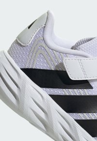 Gros plan d'une chaussure de sport blanche et noire avec dessus en mesh, bride Velcro, col rembourré et semelle texturée conçue pour le soutien et le confort.