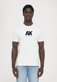 Balta medvilninė marškinėlių su apykakle ir trumpomis rankovėmis, ant priekio didelis juodas "AX" ir "ARMANI EXCHANGE" logotipas.