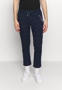 Pantalones jogger a cuadros en color azul marino, fabricados en tejido suave, con cintura elástica, cordón y detalle de bolsillo lateral con cremallera.