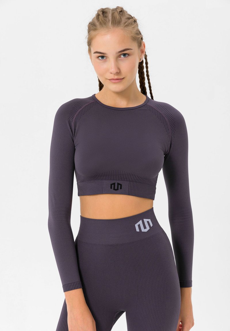 Lilla pikaaelne crop top ribimustriga ja musta logoga. Kombineeritud kõrge vöökohaga ribimustriga retuusidega, millel on hallid aktsentdetailid.