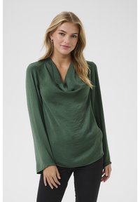 Blouse verte à manches longues avec un col drapé et un tissu léger, légèrement texturé. Présente une coupe décontractée et un éclat subtil.