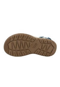 Teva sandal såle, med et brunt gummimateriale, teksturert sålemønster for grep, og en fremtredende logo preget på siden.
