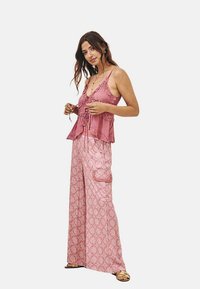 Top sin mangas rosa con bordes con volantes y lazos, acompañado de pantalones de pierna ancha con un patrón y un bolsillo tipo cargo. Sandalias planas completan el look.