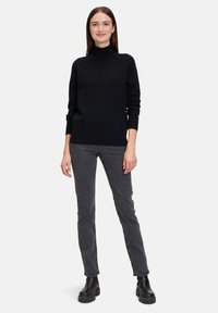 Schwarzer Rollkragenpullover mit langen Ärmeln, gestrickter Textur und geripptem Saum. Kombiniert mit grauen Jeans und schwarzen, klobigen Stiefeletten.