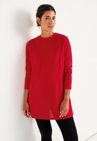 Rode geribde tuniekjurk met lange mouwen, ronde halslijn en zijsplitten, gecombineerd met zwarte leggings; gestructureerde stof.