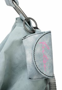 Sac bleu clair en tissu texturé avec un anneau en métal argenté et une étiquette en cuir comportant une lettrage rose et des détails de couture noirs.