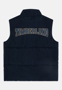 Tamnoplava puffer prsluk s visokim ovratnikom, na leđima s velikim natpisom "TIMBERLAND" u krem i tamnoplavim slovima.