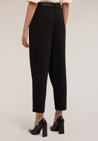 Zwarte high-waisted broek met een op maat gemaakte pasvorm, taps toelopende pijpen en een gladde textuur; gecombineerd met zwarte hoge hakken.