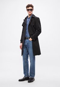 Mustast topeltrinnalise disainiga trench mantel, teksasärk, sinised teksad, must vöö ja mustad kingad. Paar suuri tumedaid päikeseprille.