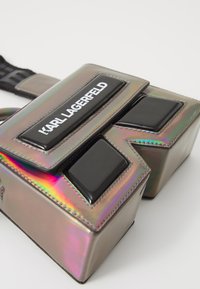 Holographic rectangular bag with black glossy accents, featuring the text "Karl Lagerfeld" on a black panel. Smooth texture. Adjustable strap.
