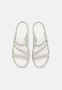 Lys grå slidesandaler med krydsseler og en hvid tekstureret sål, lavet af fleksibelt materiale for komfort.