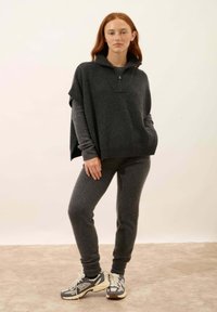 Maglione oversize grigio scuro a maglia con colletto alto e dettagli a coste, abbinato a pantaloni sportivi attillati e sneakers coordinate.