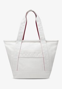 Λευκή τσάντα tote από καμβά με τριγωνικό σχήμα, διακοσμημένη με κόκκινες λεπτομέρειες στα χερούλια και στις τσέπες. Ανθεκτικό ύφασμα και μοντέρνος σχεδιασμός.