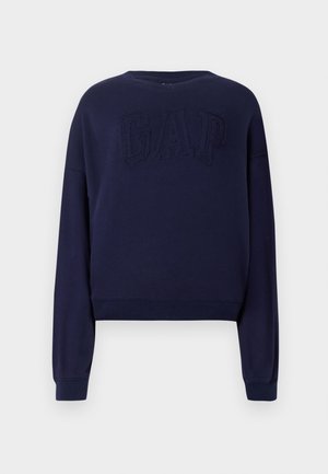 Tricou bleumarin cu gât rotund, umeri căzuți și mâneci lungi. Caracterizat prin logo-ul brodat "GAP" pe față. Textură moale.