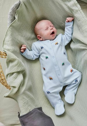 Hellblau gestreifter Baby-Overall mit Traktor-Stickerei. Aus weichem Baumwollmaterial, mit langen Ärmeln und Fußdesign, auf einer grünen Decke liegend.