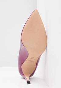 Chaussure à talon haut à bout pointu en cuir violet foncé brillant, avec une semelle en cuir nude et un talon aiguille fin, présentant un design élégant en courbe.