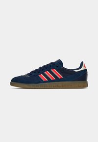 Marinblå Adidas-sneakers med röda ränder, gummisula, snörning och vit hälflik på en vit bakgrund.