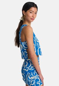 Μπλε crop top και ταιριαστή ψηλόμεση φούστα, με λευκά αφηρημένα σχέδια, χωρίς μανίκια και ανοικτές πλευρές, κατασκευασμένα από ελαφρύ ύφασμα.