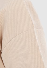 Beige-kangas, jossa on teksturoitu kuvio. Sisältää sileän sauman ja hienovaraisen kiillon. Materiaali on venyvää ja kevyttä. Sopii arkivaatteisiin.