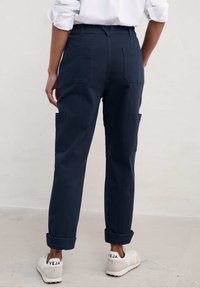 Laivaston cargo-housut suoran istuvuuden kanssa, joissa on sivu- ja takataskut, käännetyt lahkeet ja kestävä kangas. Valkoiset lenkkarit, joissa on "VEJA"-logo.