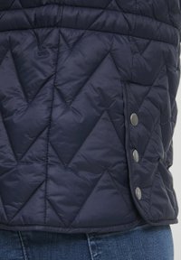 Gilet trapuntato blu navy con motivo a zigzag, texture liscia e dettagli con bottoni a pressione all'orlo. Ideale per essere indossato a strati.
