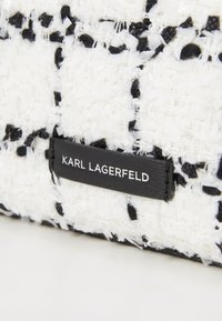 Sac en tissu texturé noir et blanc de forme rectangulaire avec une étiquette en cuir portant l'inscription "KARL LAGERFELD" embossée en argent.