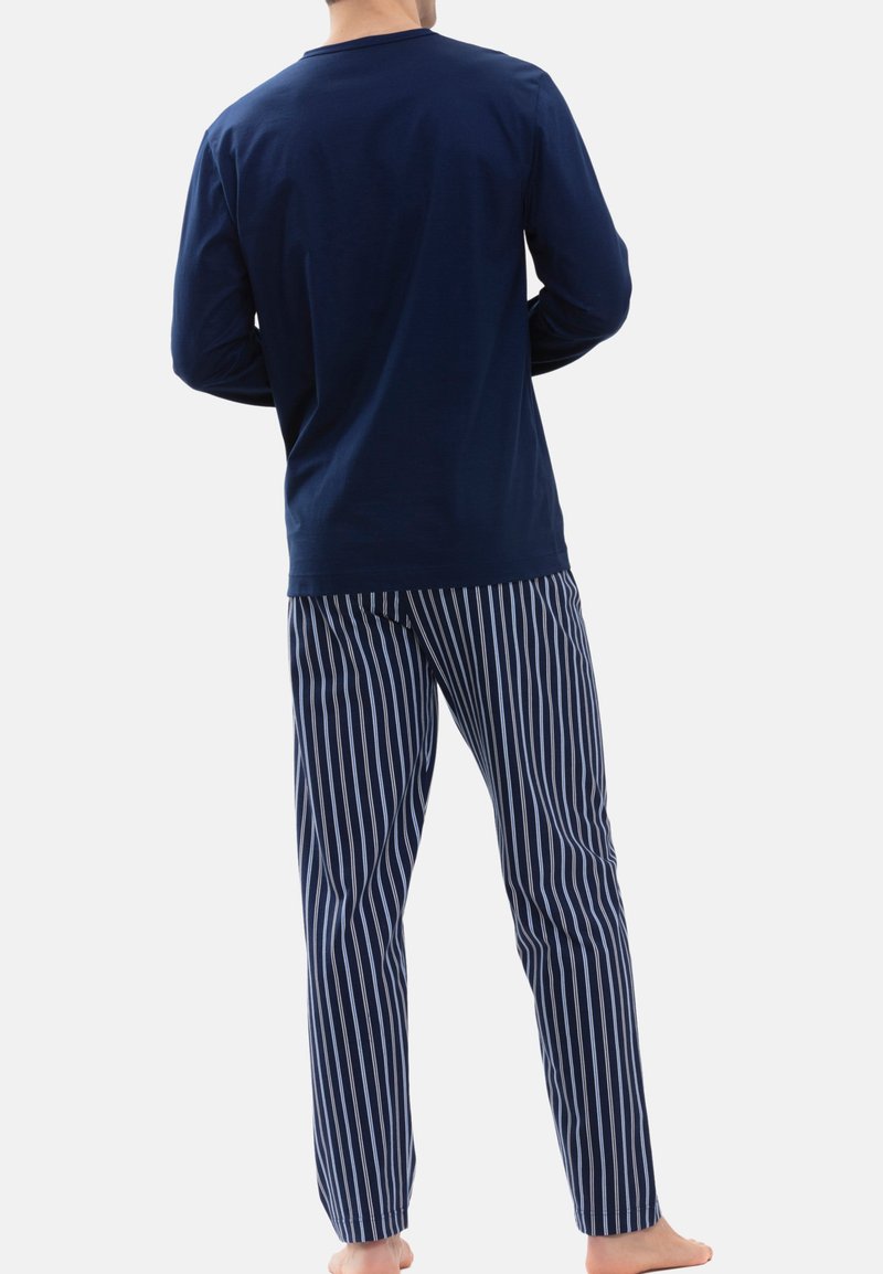 Navy blauwe lange mouw shirt met een ronde hals, gecombineerd met gestreepte pyjamabroek in navy en wit. Zachte stof, relaxte pasvorm en blote voeten.